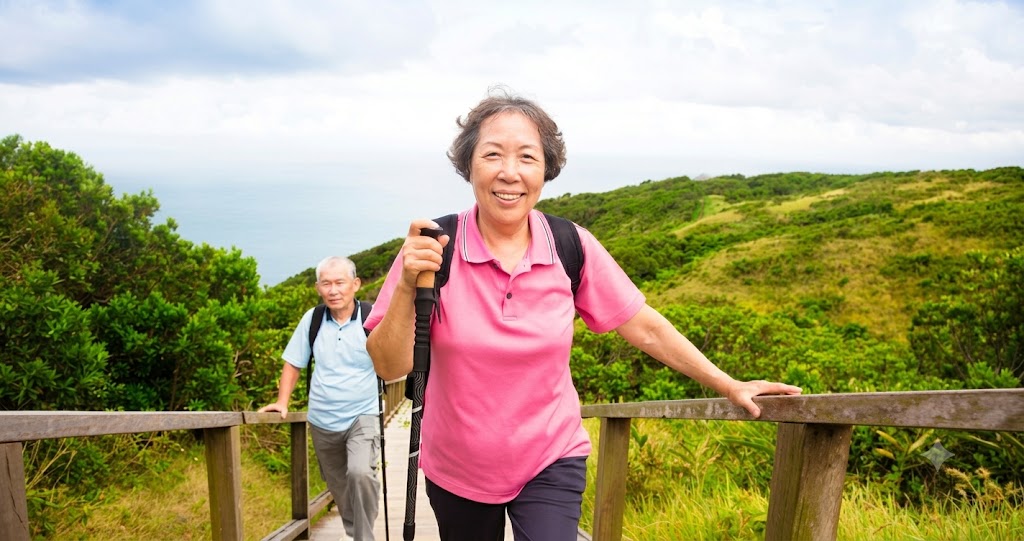 An active elderly couple hiking on a nature trail with a walking stick, illustrating the importance of mobility and access to podiatry care for Singapore's ageing population.